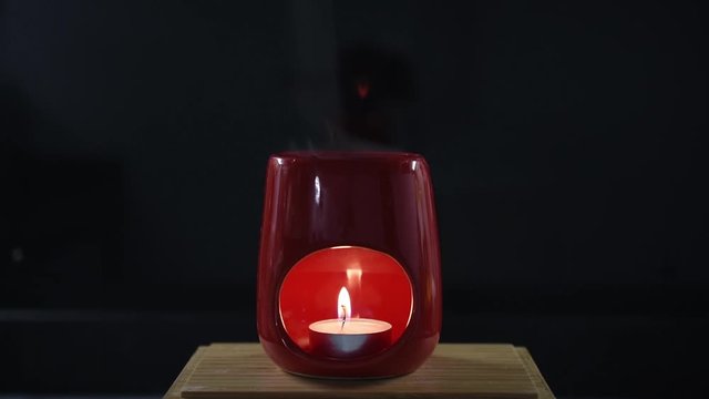 Aromatic essential oil steam /fumes coming out of a red oil burner heated by a tea light / candle. Isolated on black.