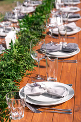 Beautifully decorated wooden table in a summer open-air cafe. Green branch and fresh flowers table decoration