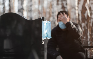 A man in a medical mask mourns, holding on to his head, sitting at the tombstone. Death from a...