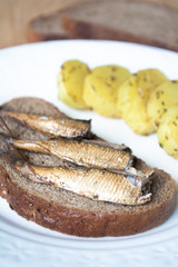 Canned sprats on rye bread served with herb baked potatoes