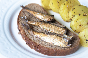 Canned sprats on rye bread served with herb baked potatoes