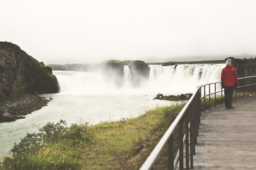 Red-coat shaped man with a woolly hat staring at the Godafoss waterfall