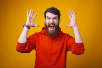 Fototapeta premium Photo of a young bearded angry man is screaming at the camera on yellow background.
