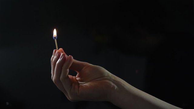 Hand holding and lighting a match against a plain black background.