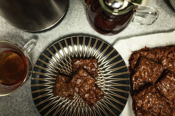 Sweet composition: chocolate brownie cake on a dark plate standing on a gray table. The concept of home baking with your own hands. Selective focus.