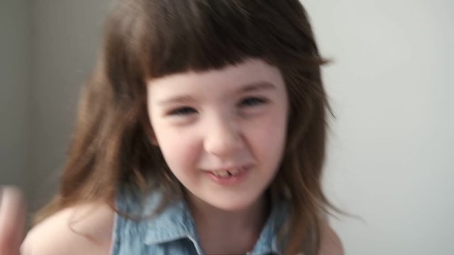 A 6-7 year old girl sings and dances while looking at the camera. Close up.