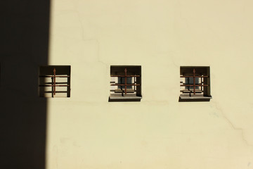 Three small windows built in plaster wall. Symmetry in building facade.