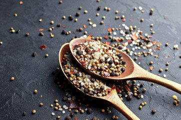 Variety of colorful spices in wooden spoons. Sea salt, mixed pepper, cardamon and mustard seeds on dark black stony table background