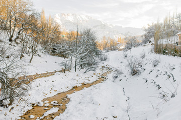 Winter snowy mountain landscape in Uzbekistan. Chimgan mountain in the distance, illuminated by the sun. Chimgansay River