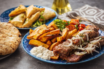 Souvlaki served with fried potatoes, tzatziki dip and pita bread, greek cuisine.