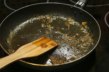 Dirty wooden pan scraper lies in black non-stick frying pan covered with large amount of fat after...
