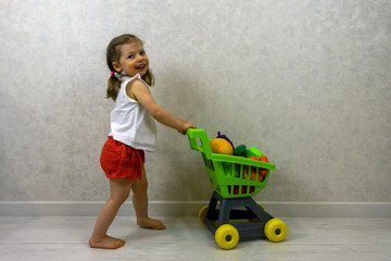 A girl is playing in a supermarket with a shopping basket full of artificial vegetables and fruits
