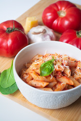 Classic italian penne pasta arabiata with its ingredients in the background: fresh tomatoes, basil, garlic and parmesan cheese