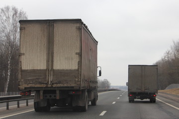A big old truck overtakes a small van, the advantages of large-capacity transport in long-distance cargo delivery at spring day