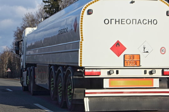 Close Up White Semi Truck Fuel Tanker With 33 1203 Dangerous Class Sign And Inscription In Russian INFLAMMABLE Moving On Asphalt Highway On A Spring Day, Side Rear View - ADR Hazardous Cargo