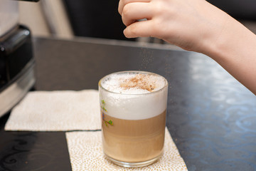 boy in a white T-shirt is preparing a hot cappuccino in a home coffee machine. sprinkled with cinnamon