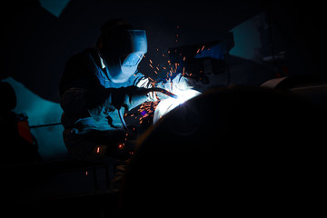 Welder at work, Pipe welding with flying sparks in the dark.