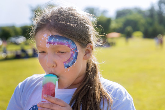Teenager with face paint eating color ice cream.