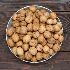 An organic walnuts in a metal tray on a dark wooden table.