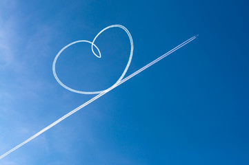 Airplane flying through clear blue sky left heart shape of vapour trails behide.