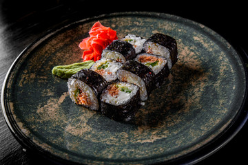 sushi roll with tuna, avocado, rice in plate on black wooden table background