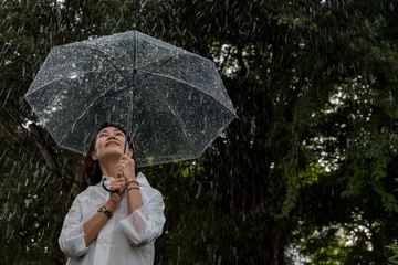 In raining day woman open umbrella stand in garden feel happyand have warmth,romantic feeling.