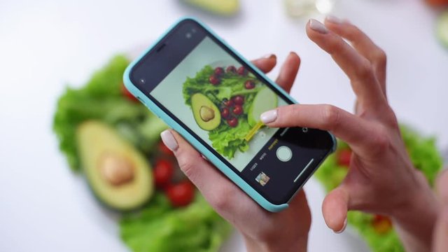 Close-up view of woman making photos vegetable salad with camera of cellphone to place pictures at social media resources. Female shooting green vegetable salad. Shooting in slow motion.