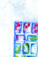 frozen red berries in ice cubes in tray on stone background space for text top view