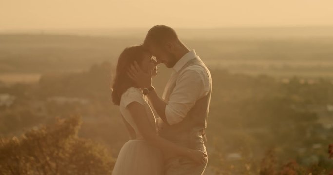 Bride and groom embracing in rural setting. Loving bride and groom standing face to face in sunlit countryside. Real-time, hand-held shot, medium shot, 4K.