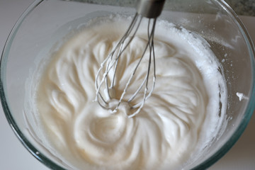 The process of whipping cream from egg whites with a mixer in a glass container, close-up