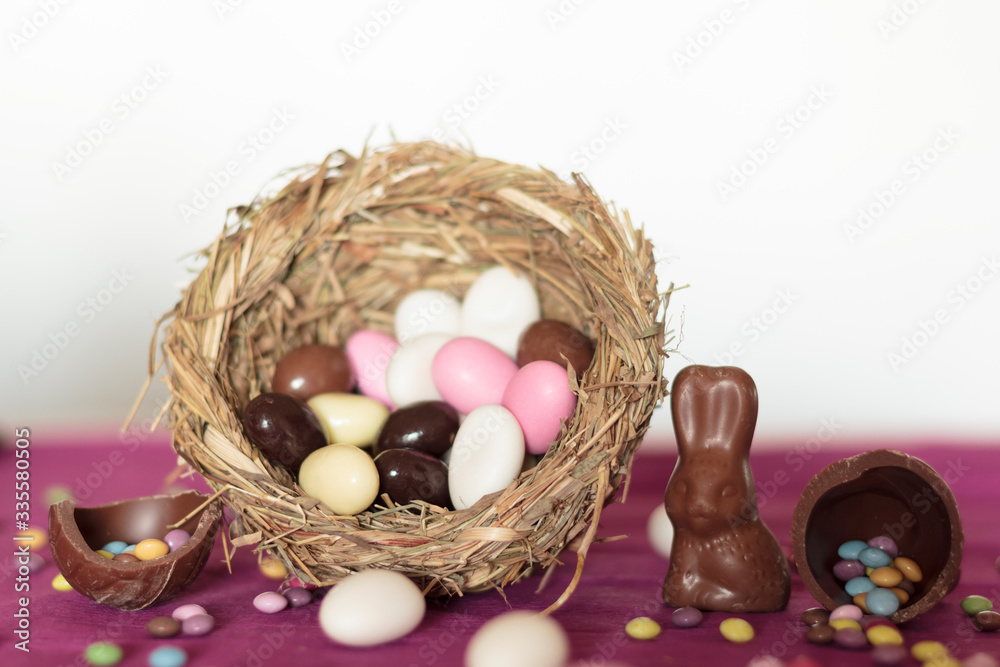 Wall mural Bird nest with easter almonds, chocolate eggs with sweets and chocolate bunny on pink table