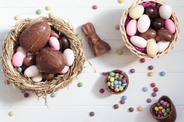 Top view of Chocolate eggs on nest, chocolate bunny, easter almonds and sweets on white wooden table. Easter composition