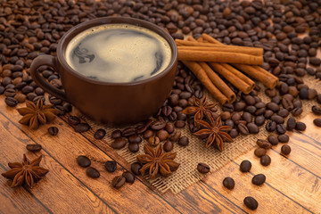 Coffee in a dark brown Cup on napkins on a wooden table with scattered coffee beans, star anise and cinnamon sticks.