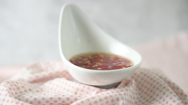 Slow motion macro of fish sauce with chili in a white cup