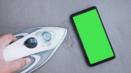 a green screen mobile phone on the ironing board. using smartphone during doing housework.