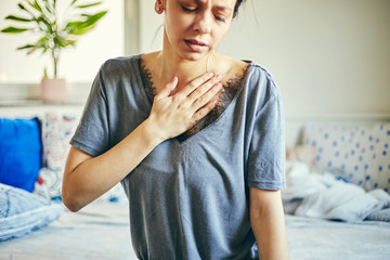 Young woman suffering from chest pain while sitting at home.