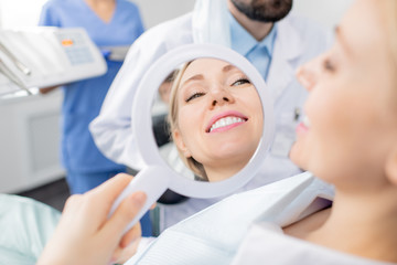 Reflection in mirror of healthy smile of pretty young smiling female patient