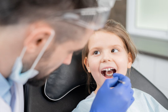 Cute Little Girl With Open Mouth Looking At Dentist During Oral Checkup