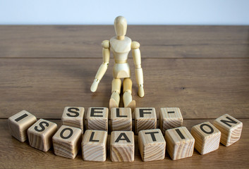 COVID-19 Pandemic Coronavirus concept ; Wooden model of a sitting man, inscription on cubes self-isolation