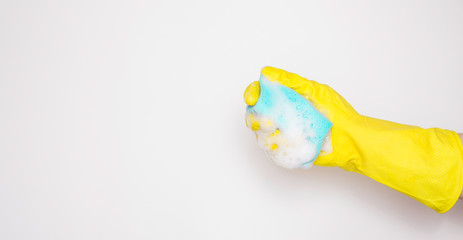 Hand in an yellow rubber glove with an blue sponge and foam on a white background. Washing dishes, cleaning, home cleaning.