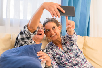 Two young women sitting on sofa at home looking at smartphone screen watching news about covid 19 coronavirus chatting on social media with family