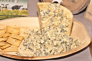 Top, front view, close distance of a wedge of Wisconsin, blue cheese with crumbles of cheese and crackers on a wood plate