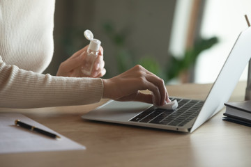 Side close up view female hands wiping working surface laptop keyboard with napkin moistened with...