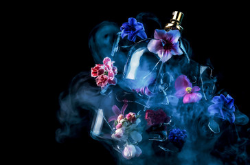 A glass perfume bottle shatters and bright spring flowers and clouds of blue and purple vapor burst out of it against a dark background - obrazy, fototapety, plakaty