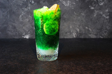 Bright, summer refreshing drink in a tall glass with crushed ice on a dark background. Top view with copy space.