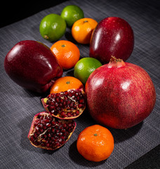 Pomegranate, tangerines, lime and apples on a dark background.