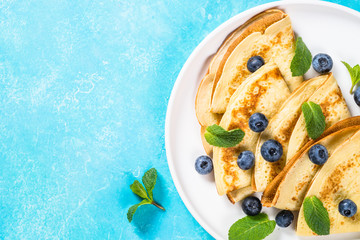 Crepes with blueberries at white table.
