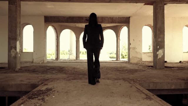 slow motion back view woman walking in abandoned classic building with big broken windows