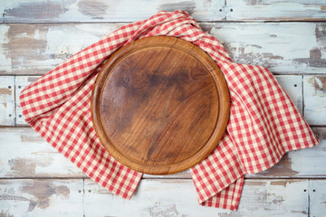 Round pizza board with red checked tablecloth on rustic wooden table Kitchen, cooking or baking mock up background for design. Top view from above