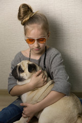 Girl hugs a pug dog. There are sunglasses on the girl. The age of the girl is 9 years.